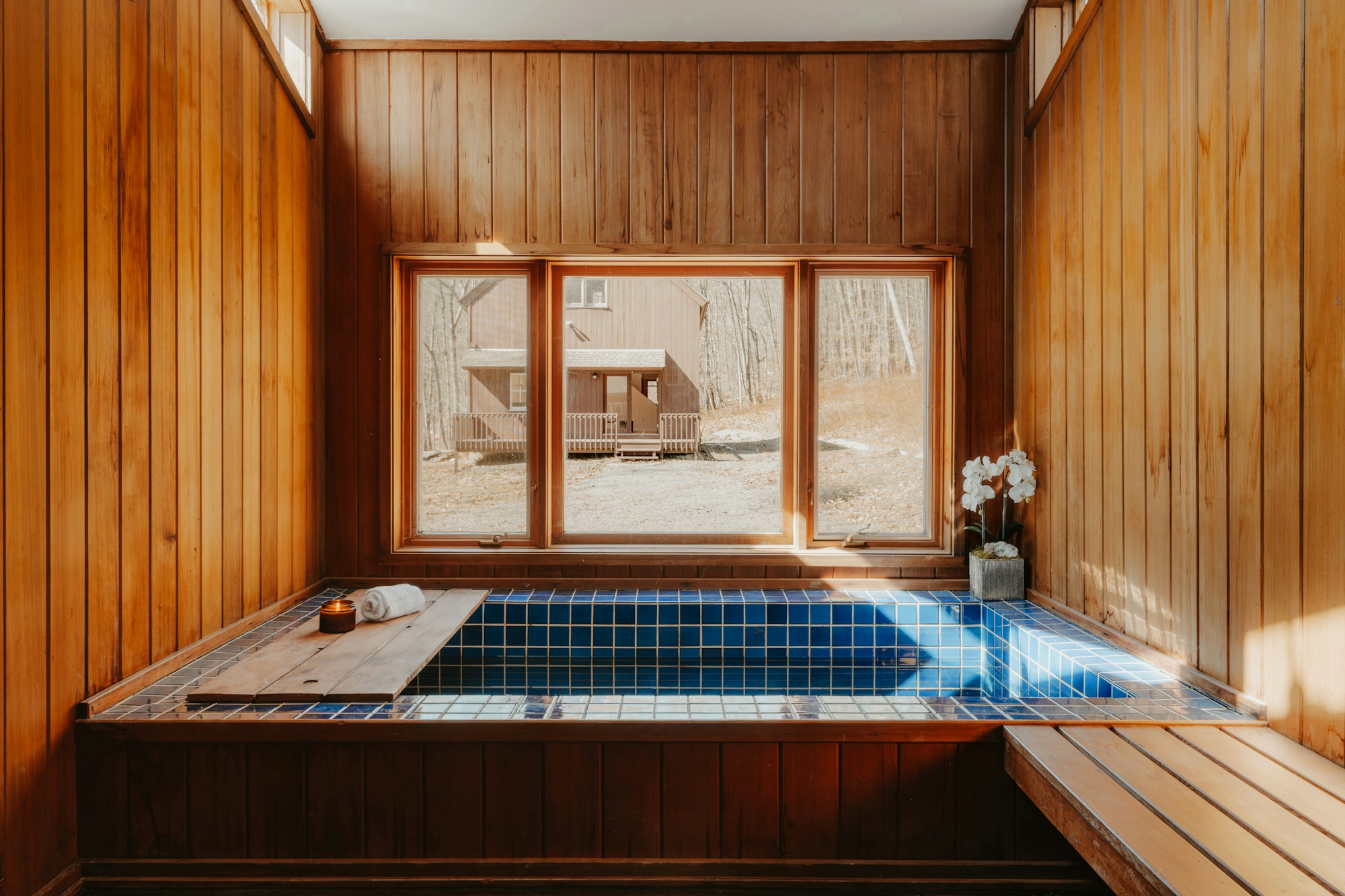 A sunlit spa interior with warm timber and a tiled bath